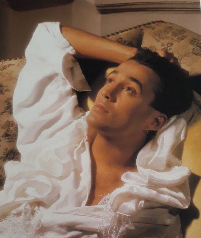 a man laying on top of a bed in a white shirt with his hands under his head