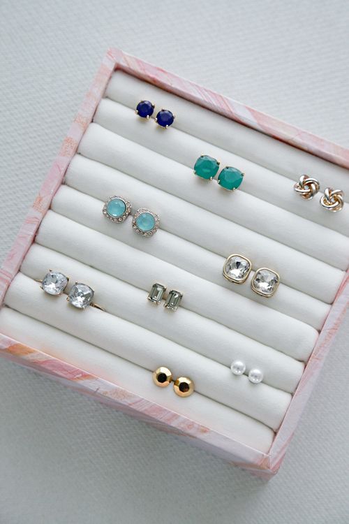 an assortment of earrings in a pink and white jewelry box on top of a table