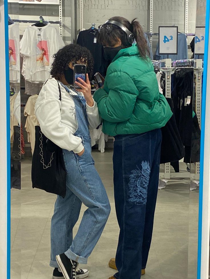 two women standing in front of a mirror looking at their cell phones and taking pictures