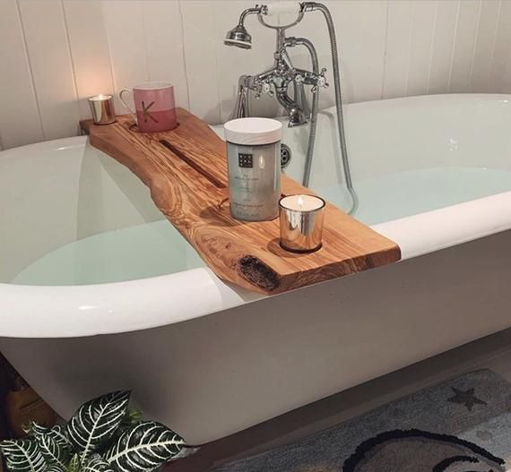 a bath tub with a wooden tray on the side and candles in front of it