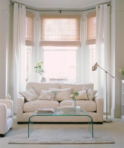 a living room filled with white furniture and windows covered in shades of light colored curtains