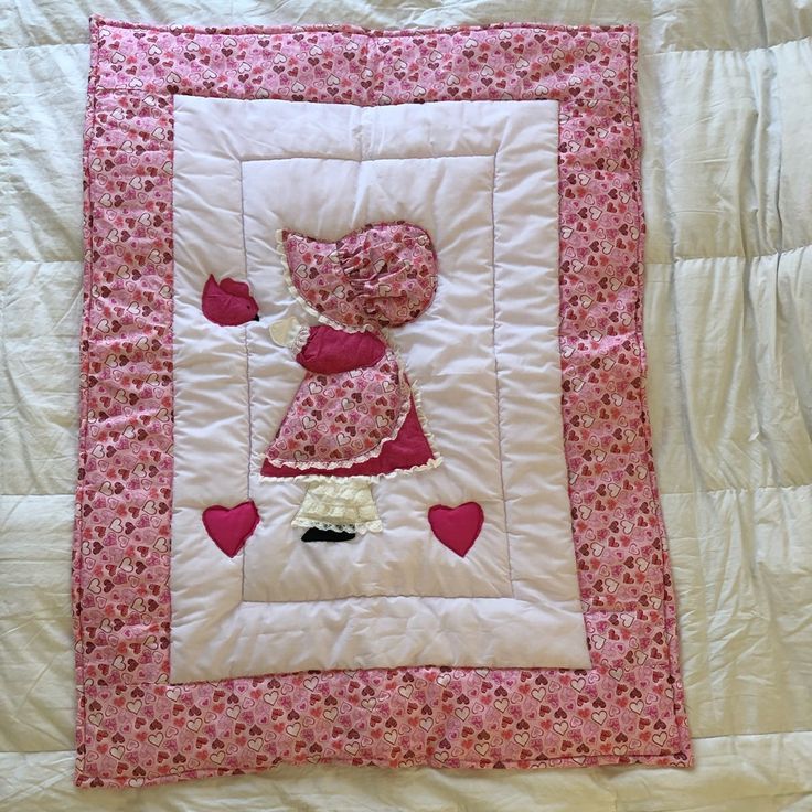 a pink and white quilted wall hanging with a teddy bear in the corner on it