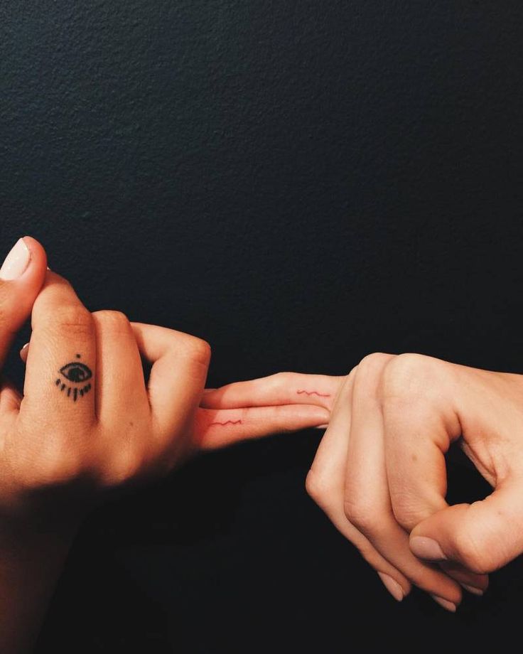 two hands touching each other with the fingers pointing towards one another and an eye tattoo on their left hand