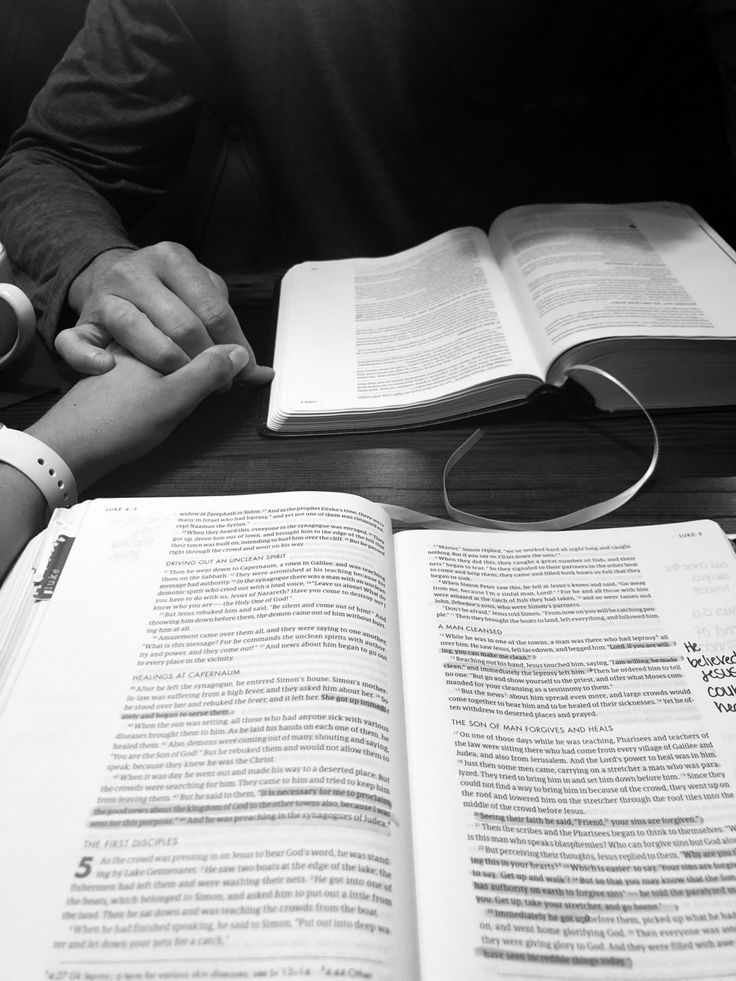 two people sitting at a table with an open book in front of them, one holding the other's hand