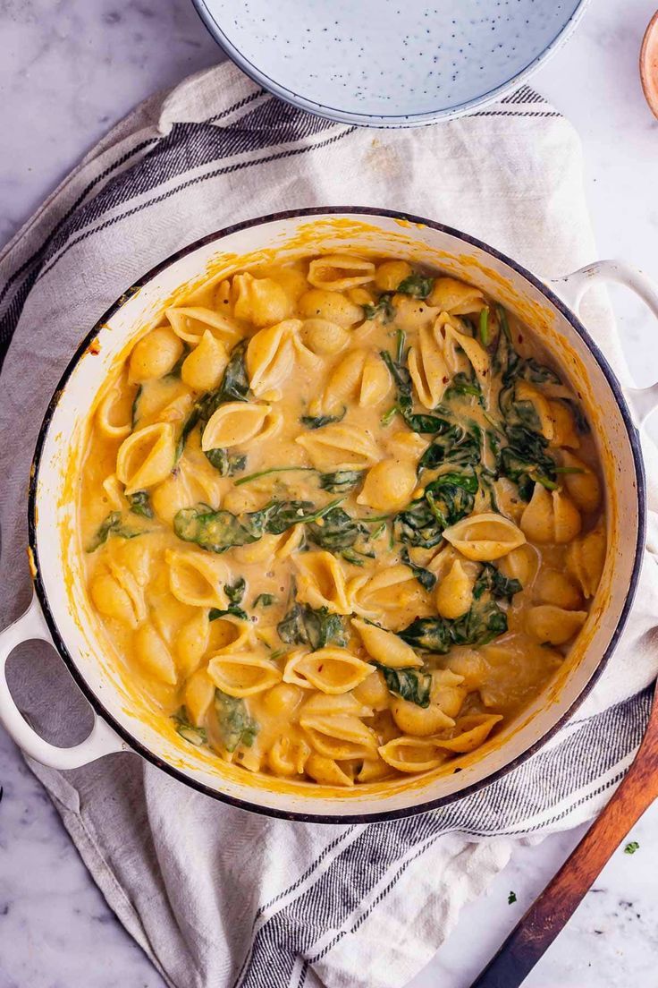 a pot filled with pasta and spinach on top of a table next to a wooden spoon