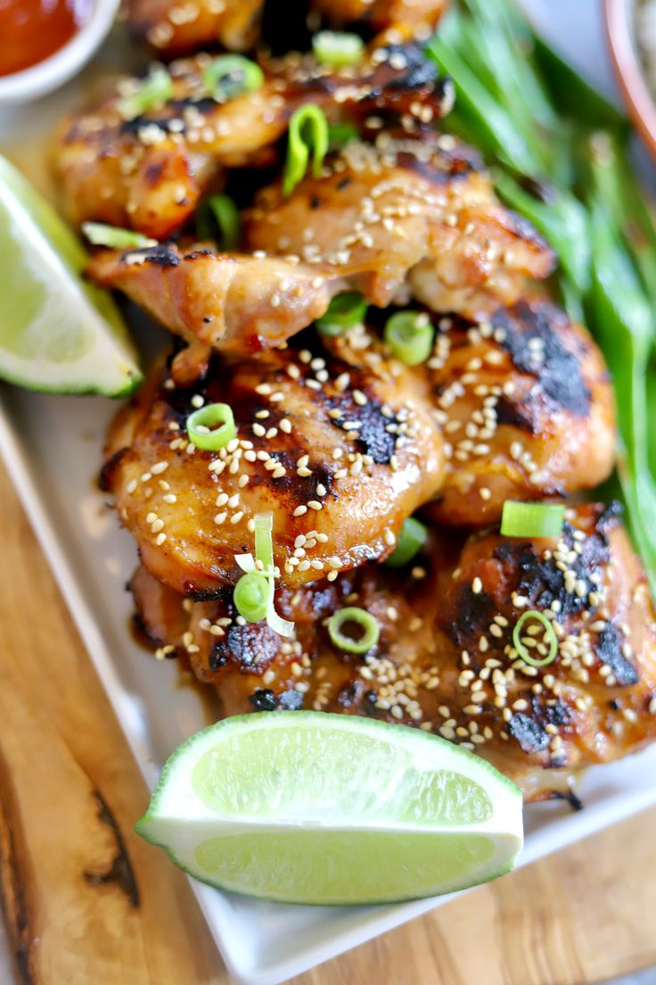 chicken wings with sesame seeds, green beans and lime wedges on a white plate