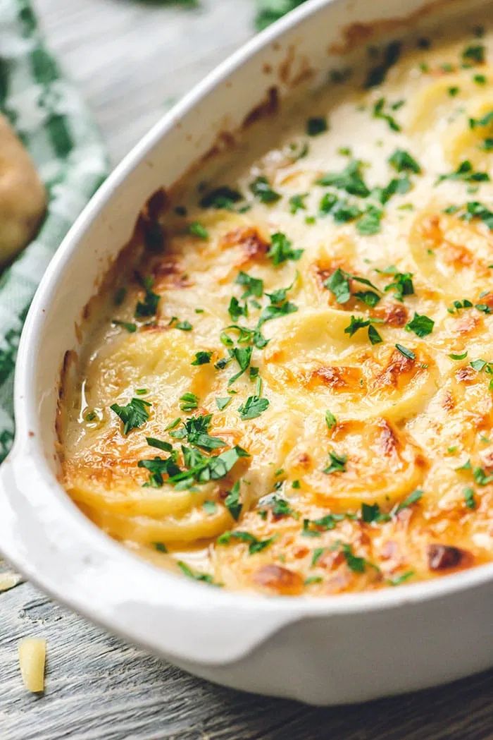 a casserole dish with potatoes and parsley in it on a wooden table