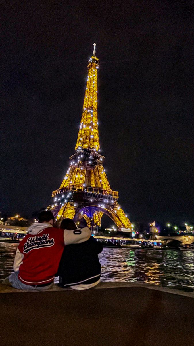 two people sitting next to each other in front of the eiffel tower at night