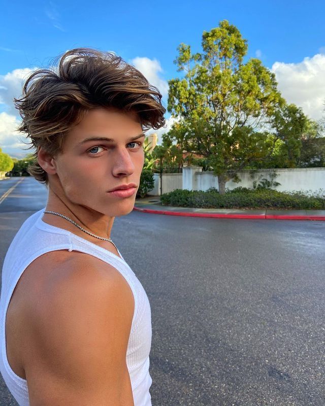 a young man standing in the middle of an empty street wearing a white tank top