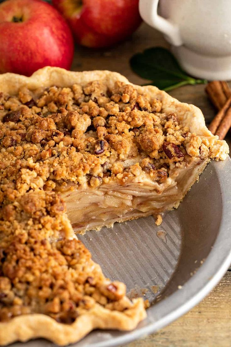 a pie on a plate next to apples and cinnamon sticks