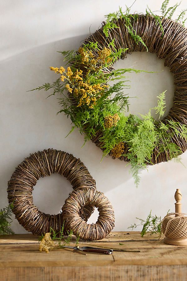 two wicker wreaths are sitting on a table next to some plants and scissors