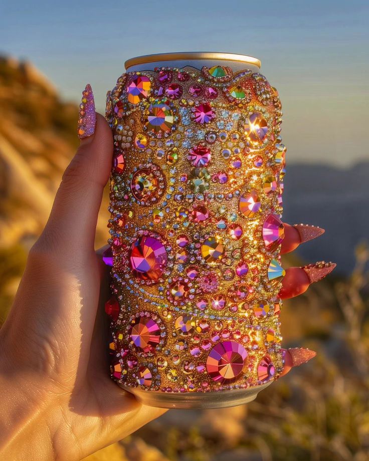 a hand holding up a can covered in lots of colorful jewels and crystals on the side of a mountain