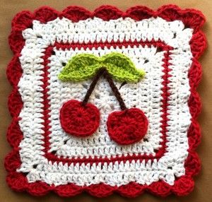 a crocheted square with cherries and leaves on the side, in red and white