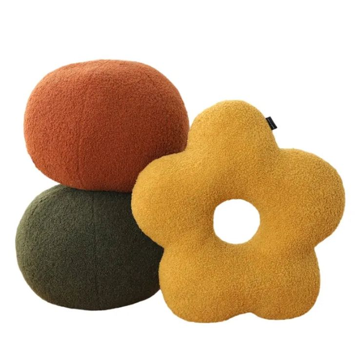 three different colored pillows sitting next to each other on a white surface, one with an orange flower in the middle