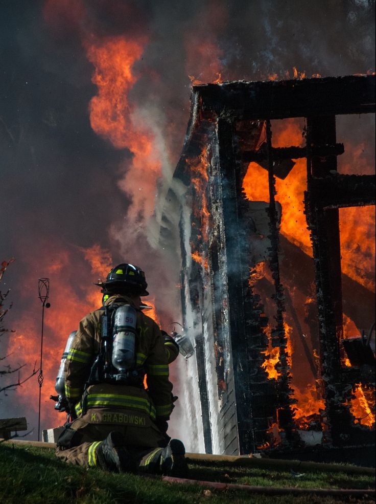 a firefighter squatting down in front of a building that has been consumed by flames