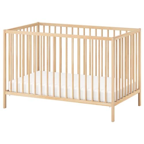 a wooden crib with white sheets on the bottom and side, in front of a white background