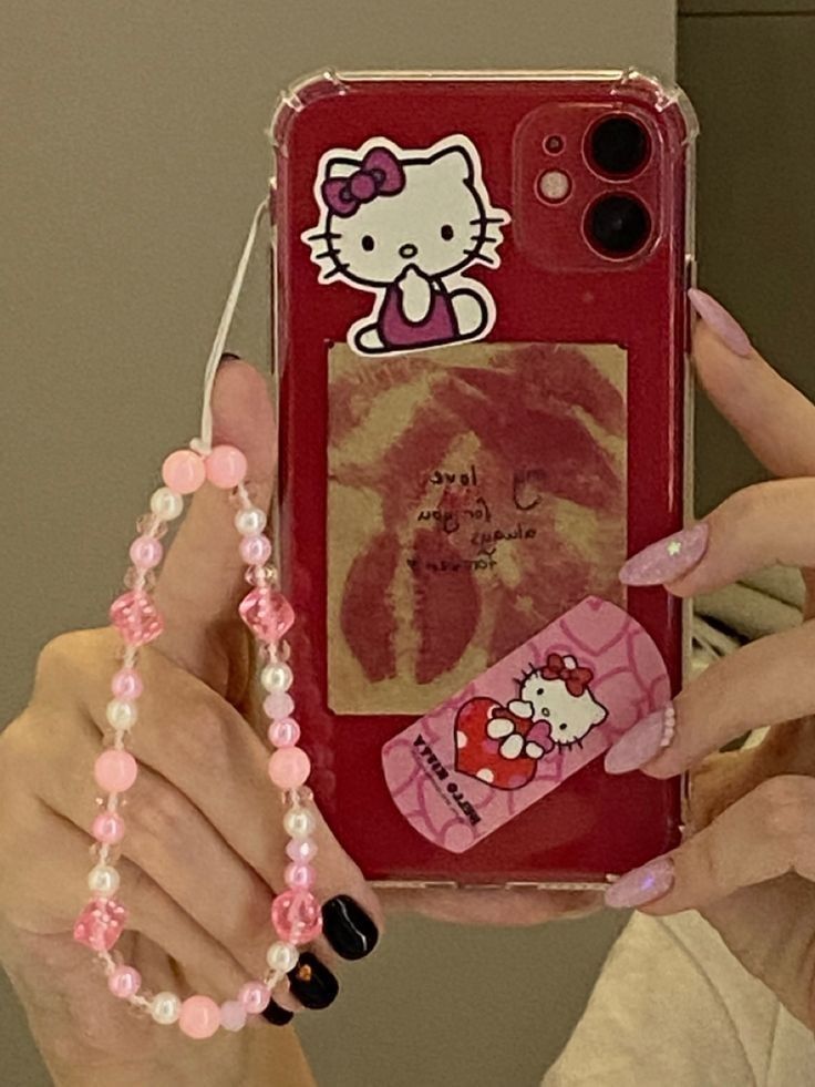 a woman holding up her phone case with hello kitty stickers on it