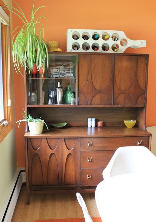 a wooden cabinet sitting next to a white bath tub in a room with an orange wall