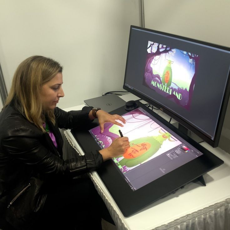 a woman sitting at a desk drawing on a large screen