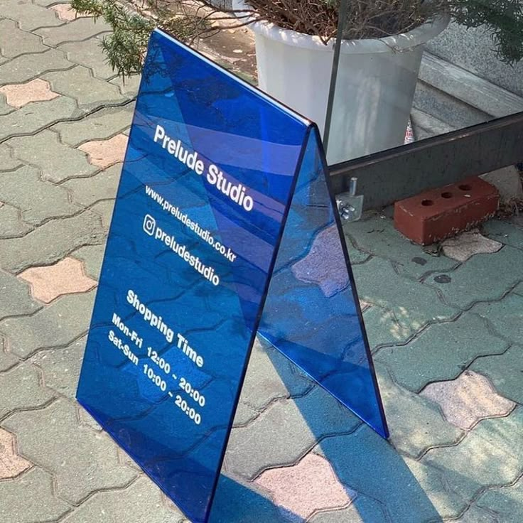 a blue sign sitting on the side of a road next to a potted plant