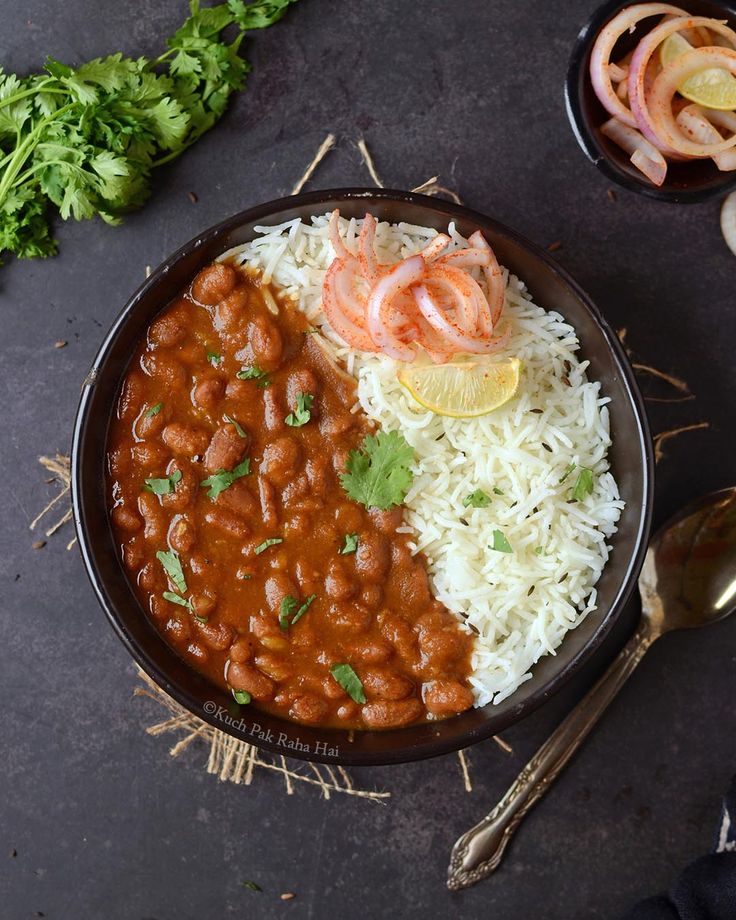 a bowl filled with rice and beans on top of a black table next to silverware