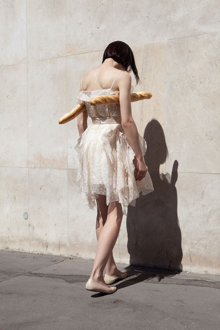 a woman in a white dress is walking down the street with a stick on her back