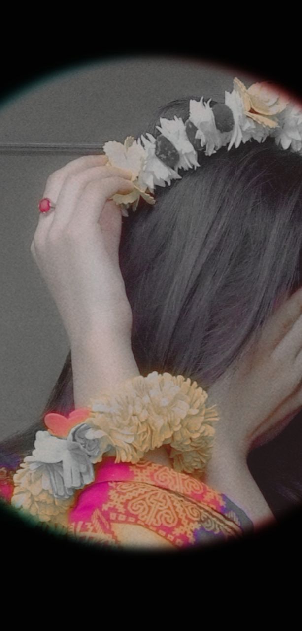 a woman wearing a flower crown holding her hair up to her face with both hands