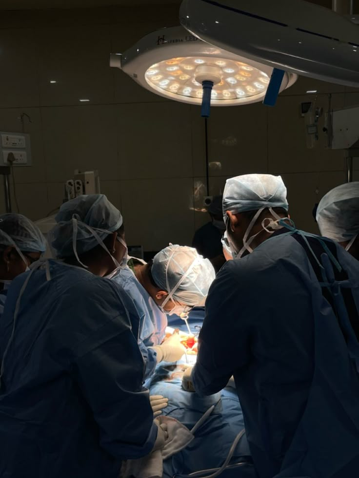 doctors performing surgery in an operating room with lights on and medical staff standing around them