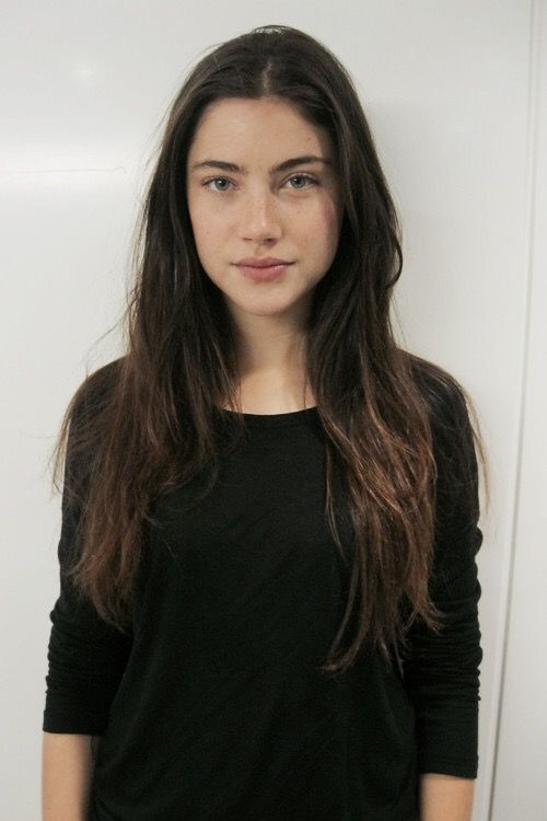 a girl with long hair standing in front of a white wall and looking at the camera