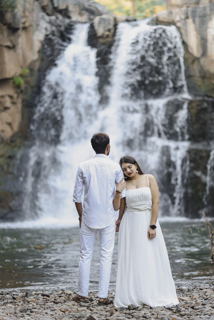 a man and woman standing in front of a waterfall