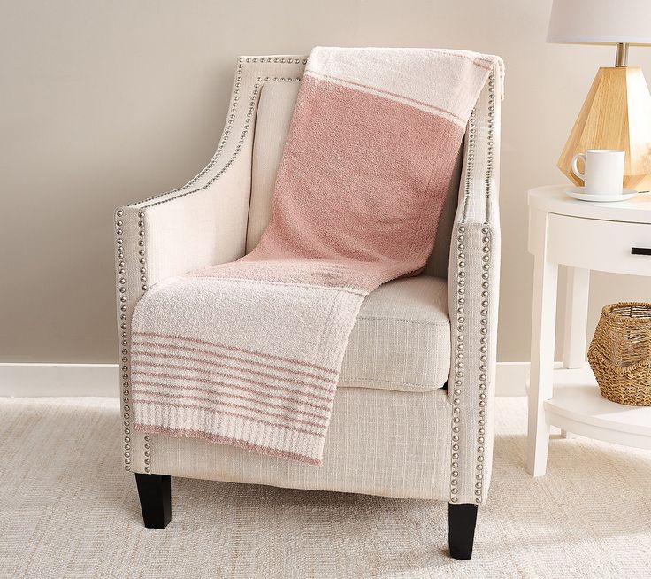 a white chair with a pink blanket on top of it next to a table and lamp