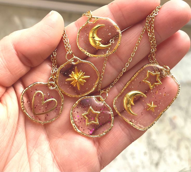 the hand is holding four different necklaces with stars and moon designs on them,