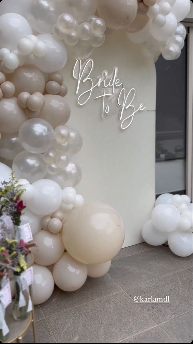 the entrance to a bridal to be event with white balloons and flowers on it