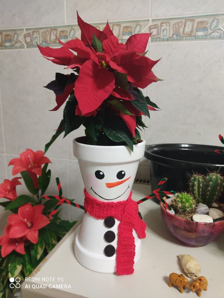 a potted plant with a snowman face on it and poinsettis in the background