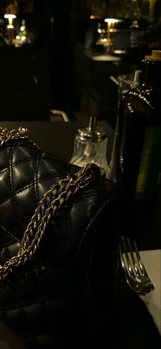 a black purse sitting on top of a table next to a fork and bottle filled with liquor