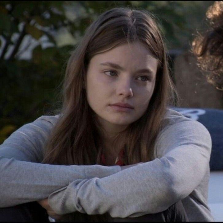 two young women sitting next to each other in front of a car and one is looking at the camera