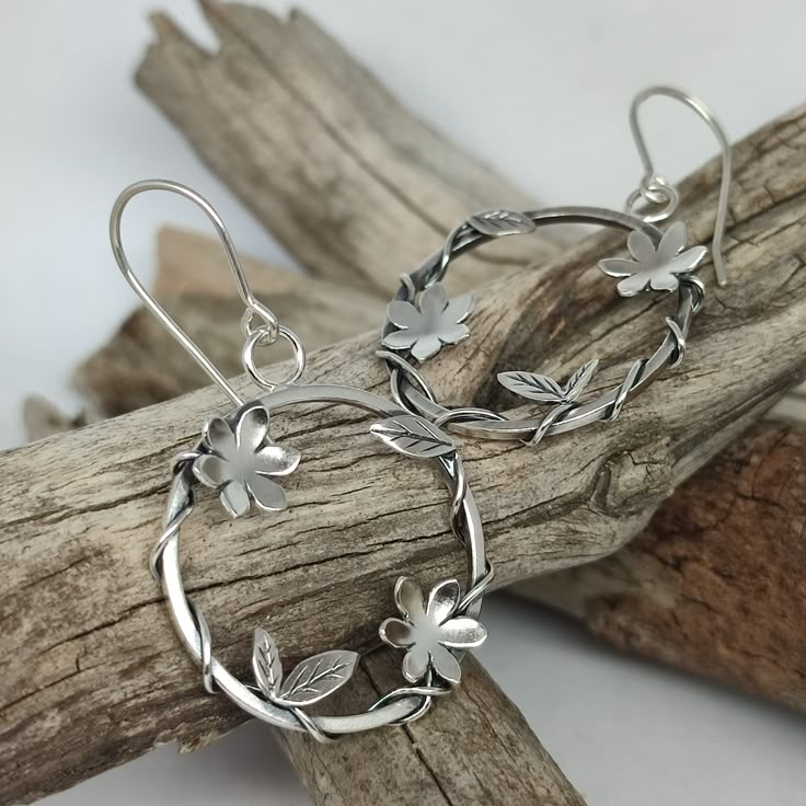 Floral sterling silver hoop earrings. Flowers and Leaves hoop earrings. Nature earrings. Plants hoop earrings. Metalsmith. Silversmith  Handmade earrings in my workshop in Barcelona. The base is a square thread of 1.25 mm and 2.6 mm in diameter in a circular shape. The flowers and leaves are drawn and cut by hand from sheet metal. I then sand down the leaves and flowers and attach the sterling silver stem which is then wrapped around the hoop to resemble a plant growing around the hoop. They are lightly oxidized to create contrast and depth, and finished in a satin gloss. These are a delicate earrings with a special design that can look at any situation. 2.6 cm diameter and 4 cm high . Hook closure. Look in my shop. https://www.etsy.com/shop/TereReyesJoies/items The shipment varies by coun Metalsmithing Jewelry Earrings, Metal Flower Earrings, Unique Silver Earrings, Silver Clay Jewelry Ideas, Metal Jewelry Handmade, Metal Sheet Design, Handmade Silver Earrings, Silversmithing Jewelry, Sterling Silver Earrings Handmade