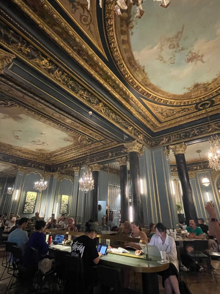 several people sitting at tables in a room with gold and blue paint on the ceiling