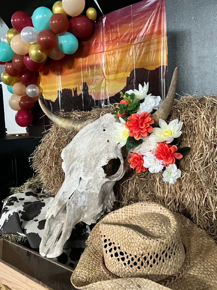 a cow skull, straw hat and balloons are on display in a room with hay bales