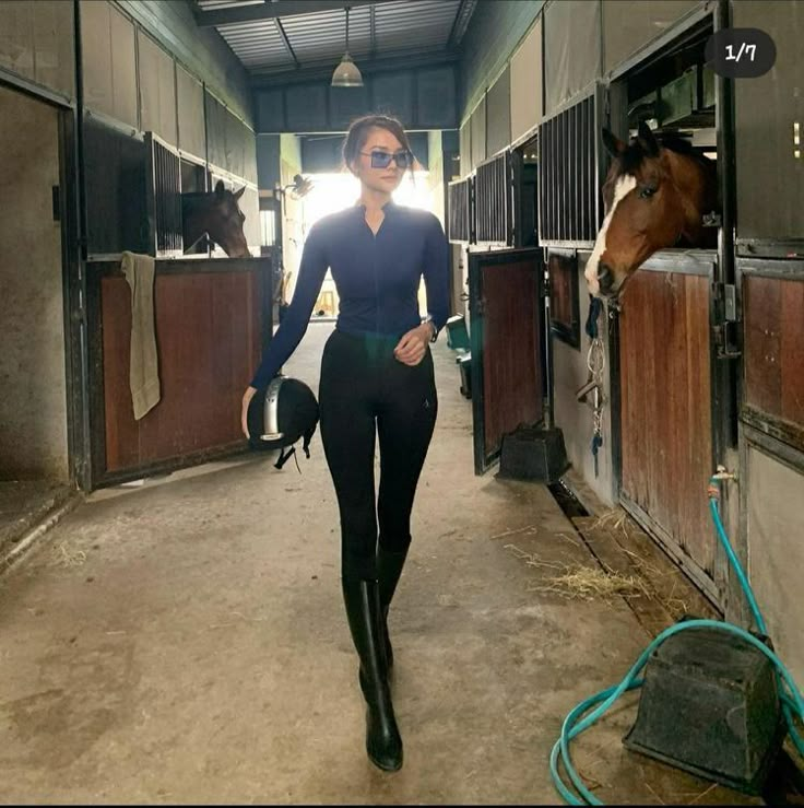 a woman walking down a hallway with horses in the backgrouds and wearing riding boots