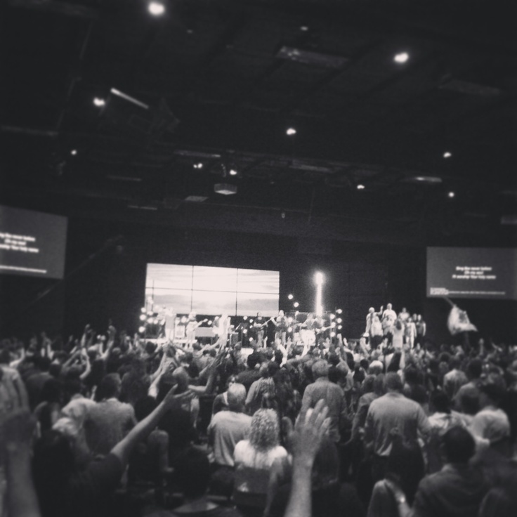 a large group of people standing in front of a stage with their hands up to the sky