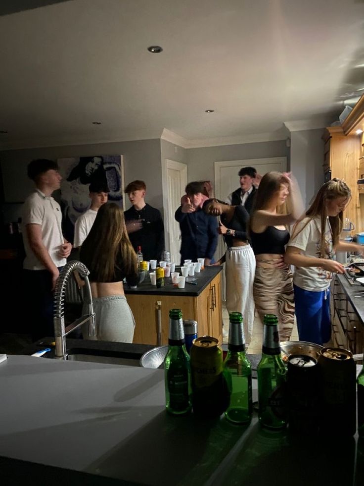 a group of people standing in a kitchen next to bottles on the counter and sink