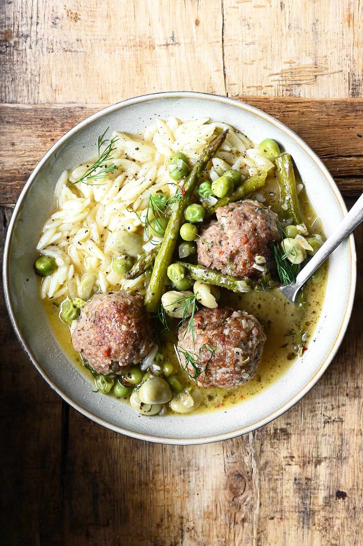 a white bowl filled with meatballs, rice and asparagus on top of a wooden table