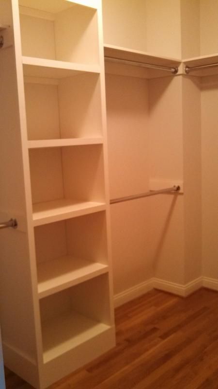 an empty walk in closet with white shelving and wood flooring on the side