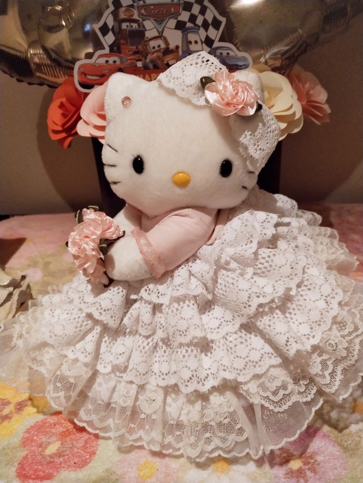 a hello kitty doll sitting on top of a bed next to some balloons and flowers