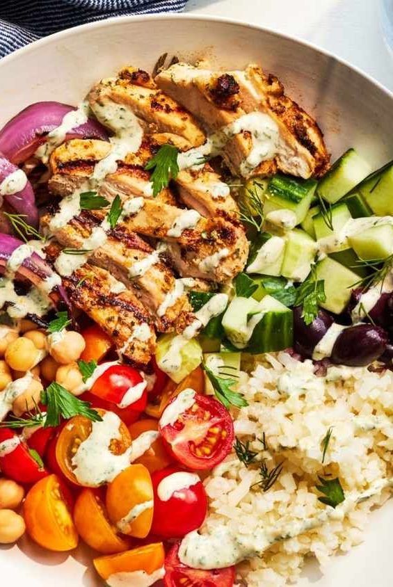 a white plate topped with chicken, rice and veggies next to cucumbers