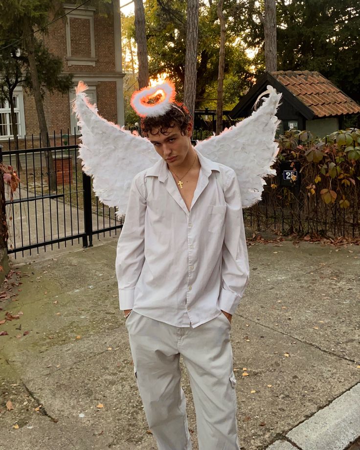 a man in white shirt and angel wings standing on sidewalk