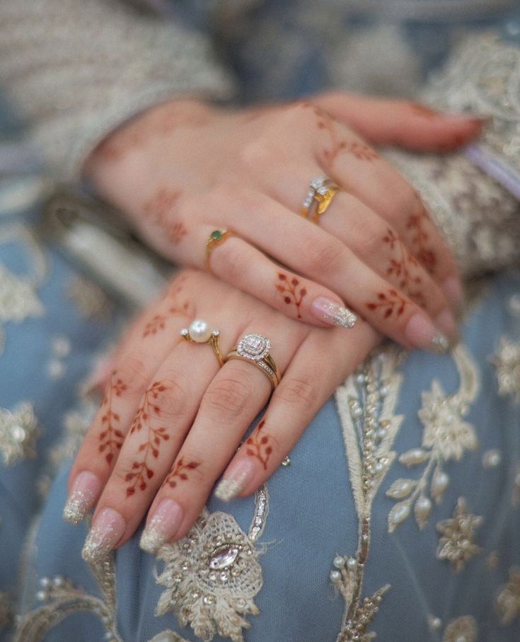 a woman's hands with hennap and rings on her fingers, sitting in a blue dress