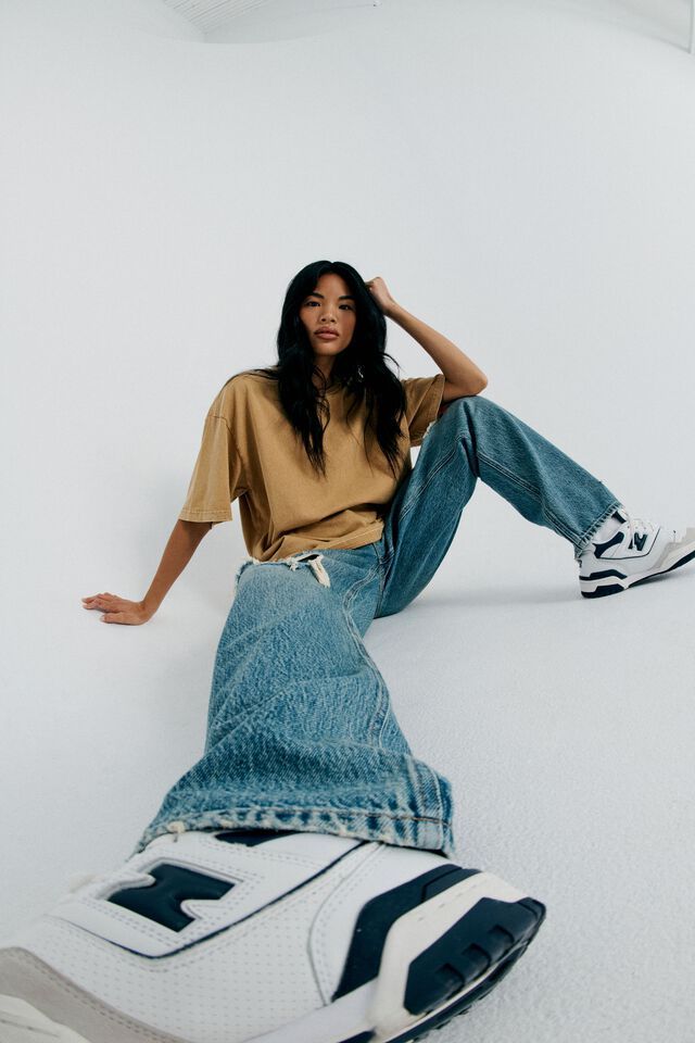 a woman sitting on the ground with her legs crossed and wearing jeans, a t - shirt and sneakers