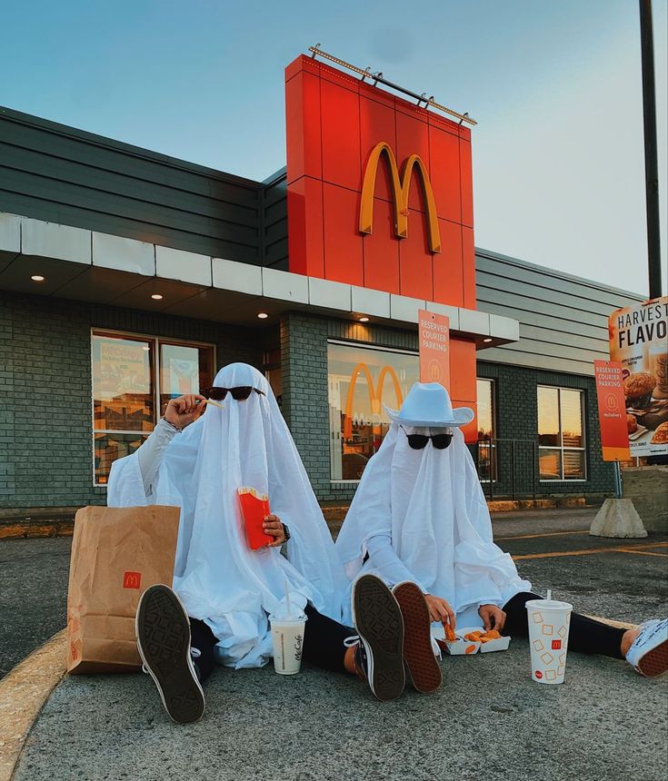 two people dressed in white sitting on the ground with their feet propped up and eating